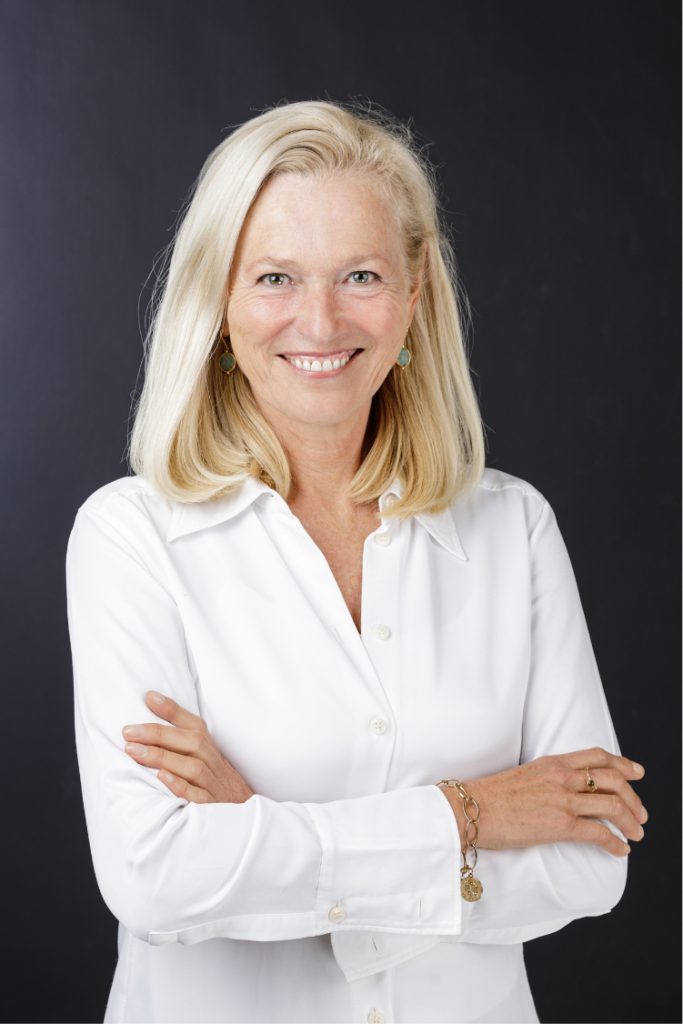 Anke Huppertz, initiatiefnemer van Laat Leven, lachend in een witte blouse met gekruiste armen voor een donkere achtergrond.